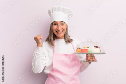 middle age woman feeling shocked,laughing and celebrating success. baker and cakes concept