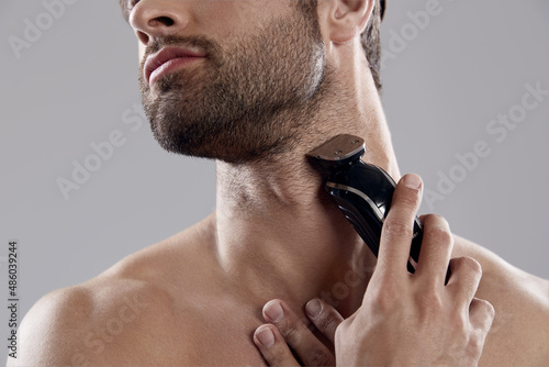 Young man shaving beard with electric razor