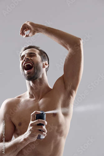 Excited man applying deodorant on his body