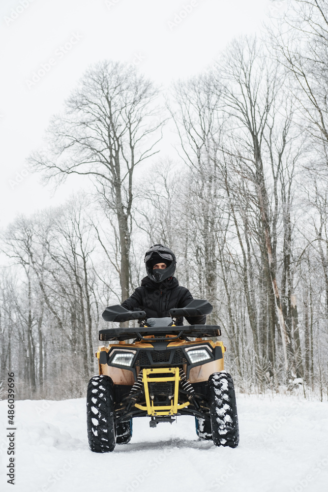 Hero shot of a man on a quad bike in winter background. Portrait of a quadricycle rider in snowy forest