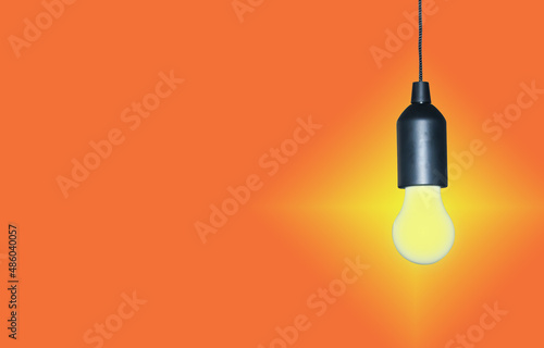 A light bulb suspended on a black wire isolated on an orange background.