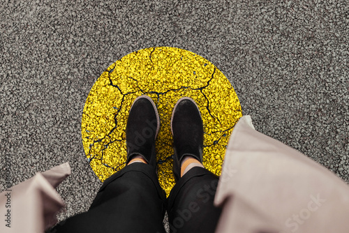 Woman legs in black shoes stands on a yellow circle of the road, top view. Leave your comfort zone for personal development photo