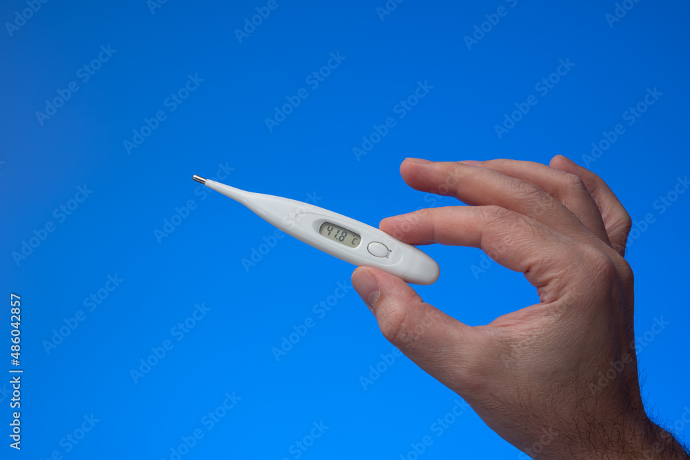 Plastic thermometer held in hand by Caucasian male. Close up studio shot, isolated on blue background Plastic thermometer held in hand by Caucasian male. Close up studio shot, isolated on blue background