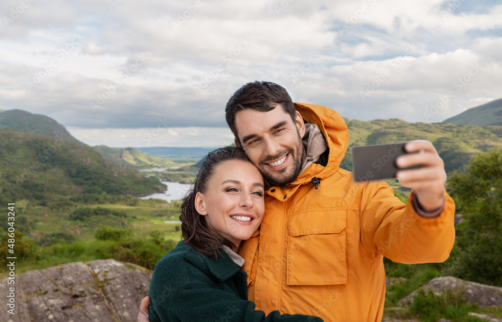 technology, travel and travel concept - happy couple with smartphone over river valley at Killarney National Park in ireland on background