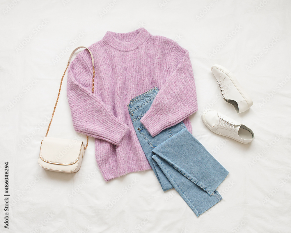 Lilac knitted sweater blue jeans white sneakers and bag lie on white background. Overhead view of woman s casual outfit. Trendy stylish women clothes. Flat lay top view. Stock Photo Adobe Stock