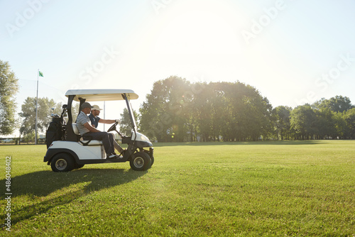 Golfers ride golf cart on golf field at sunny day