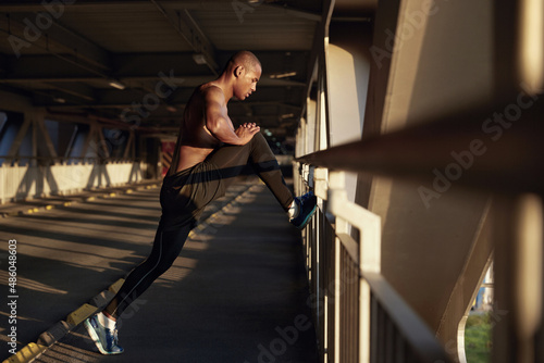 Young black sportsman stretching on empty bridge