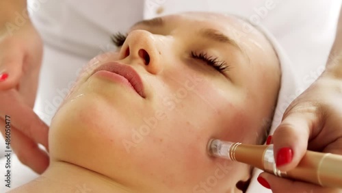 Beautician cosmetologist doing procedure fractional microneedle mesotherapy with Dermapen. Hardware cosmetology in clinic salon for client.  photo