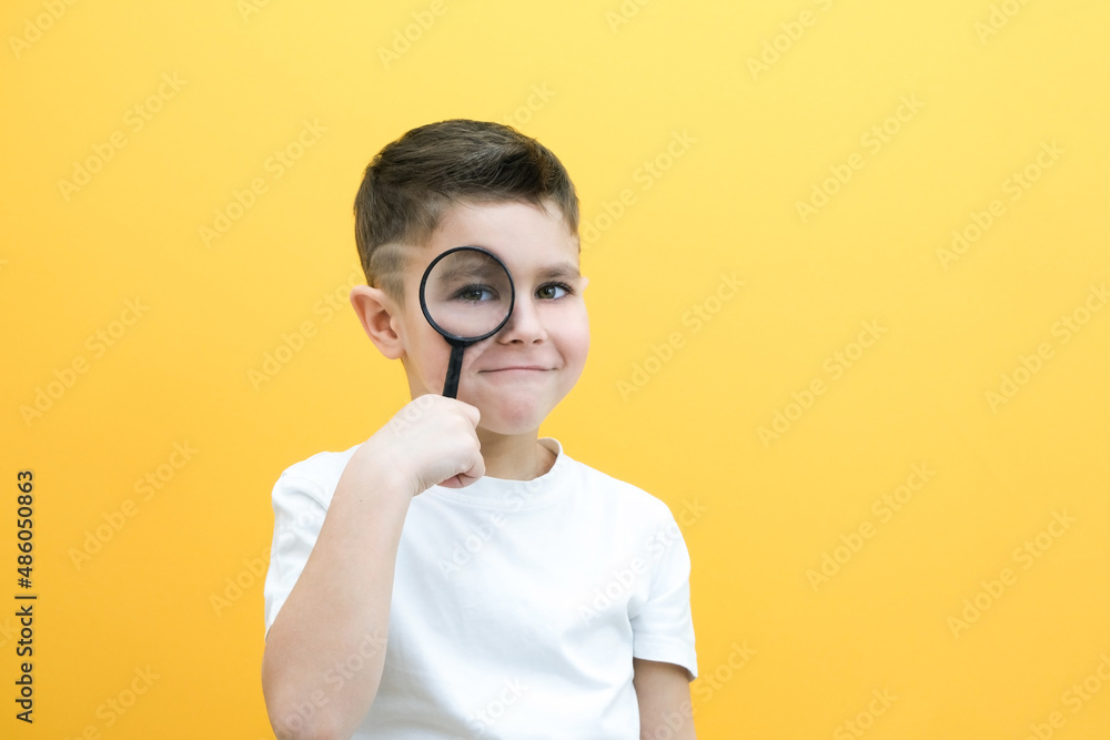 Positive curious schoolboy in casual clothes looks at the camera through a magnifying glass Positive curious schoolboy in casual clothes looks at the camera through a magnifying glass