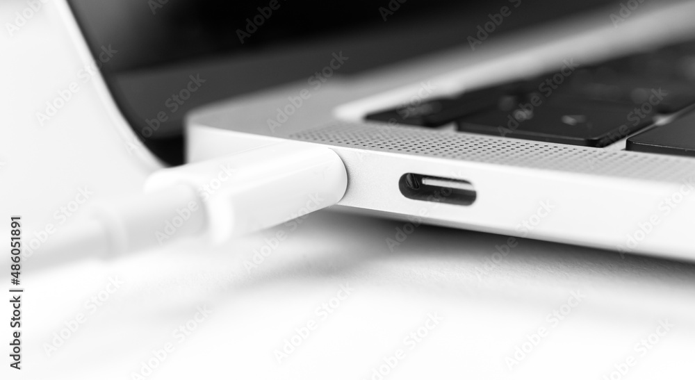 Charging battery laptop. Modern USB C port for fast charge. White cable plugged in laptop close-up view photo Charging battery laptop. Modern USB C port for fast charge. White cable plugged in laptop close-up view photo