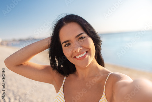 people, summer and swimwear concept - happy smiling young woman in bikini swimsuit taking selfie on beach