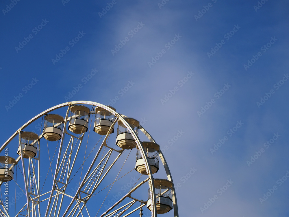 close up of a white ferris wheel with enclosed gondola cars against a bright blue sky