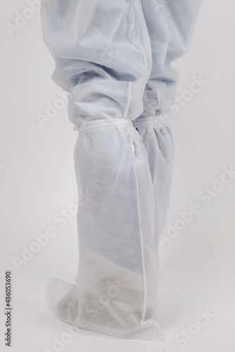 Nurse wears disposable gown and disposable shoes cover. Doctor putting on white medical shoe covers, closeup. Clothes for hospital visits or medical uniform concept. Overshoes protection.
