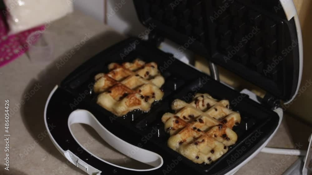 A woman opens a heated waffle iron and checks the degree of readiness of the waffle. Closes the waffle iron. Breakfast preparation. Close-up. A woman opens a heated waffle iron and checks the degree of readiness of the waffle. Closes the waffle iron. Breakfast preparation. Close-up.