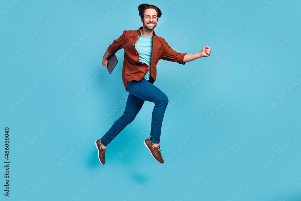 Full length photo of cool brunet millennial guy run with laptop wear eyewear shirt trousers sneakers isolated on blue background