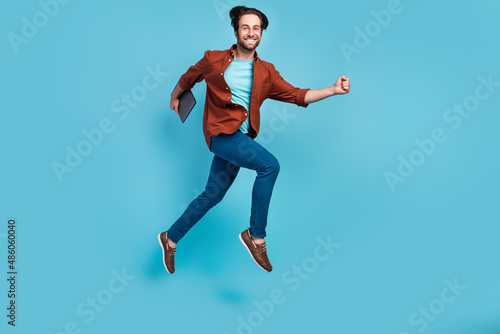 Full length photo of cool brunet millennial guy run with laptop wear eyewear shirt trousers sneakers isolated on blue background © deagreez