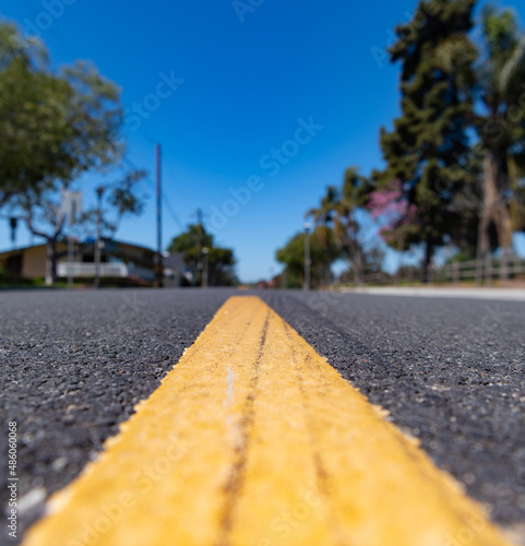 Single yellow line road marking on asphalt road along blurry residential street in suburbs