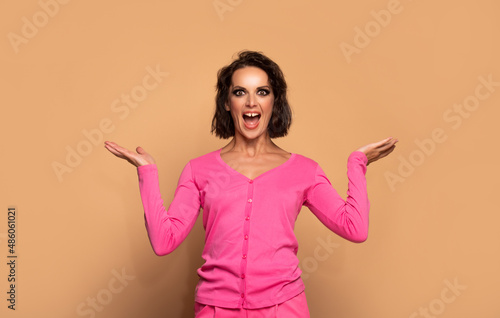 Shocked woman in fashion pink sweater showing open hands for copy space, presenting product