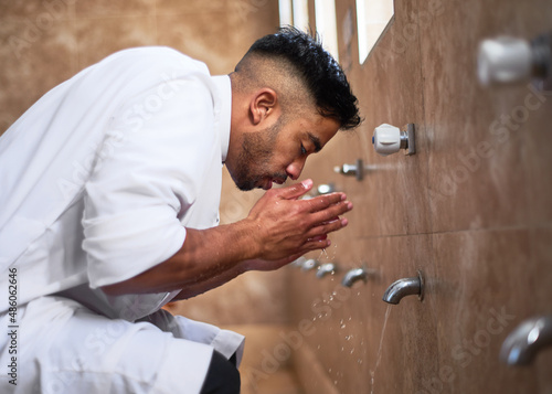 A young Muslim man performs wudu during prayers at a mosque by cleansing his face in the washroom photo
