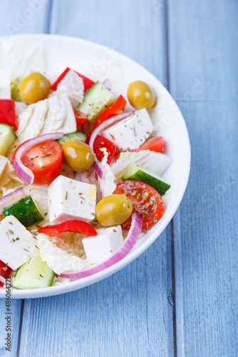 Greek salad. Traditional Greek dish. Healthy vegetarian food. Fresh vegetables and feta cheese in a white plate. Close-up, blue background.