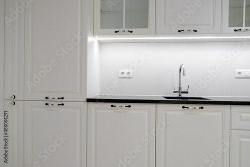 Modern and elegant kitchen with white drawers and cupboards, black marble countertop and built-in sink with silver tap