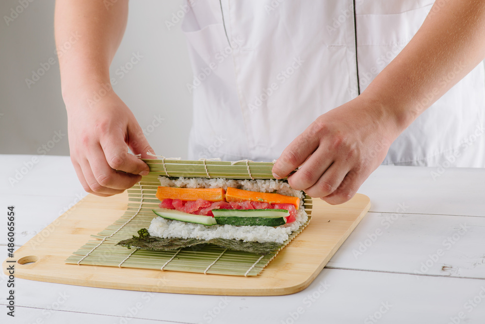 the chef cook prepares sushi and wraps a letter to the nori in the roll, on white background the chef cook prepares sushi and wraps a letter to the nori in the roll, on white background