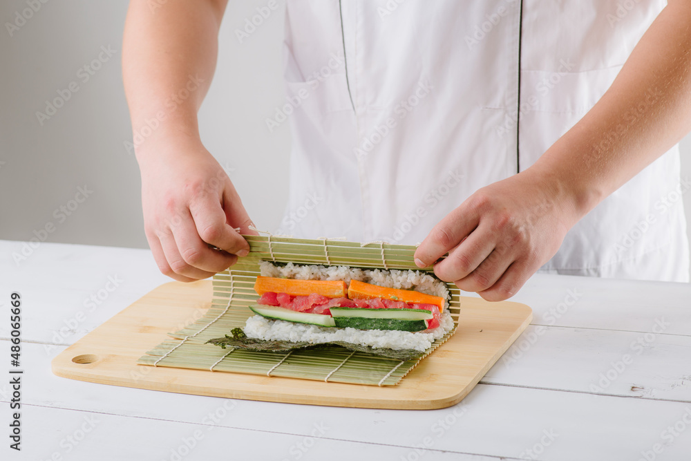 the chef cook prepares sushi and wraps a letter to the nori in the roll, on white background the chef cook prepares sushi and wraps a letter to the nori in the roll, on white background