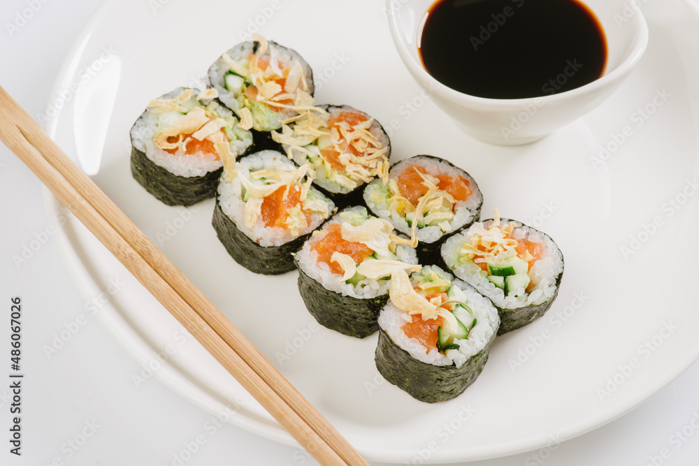 Sushi with chopsticks on a white plate. Sushi roll japanese food in restaurant isolated on white background. Fresh hosomaki pieces with rice and nori. Sushi with chopsticks on a white plate. Sushi roll japanese food in restaurant isolated on white background. Fresh hosomaki pieces with rice and nori.