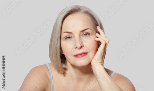 Fifty year old woman is very pleased with her well-groomed face relaxed looking at the camera. Macro face. Realistic images with their own imperfections. Isolated on grey.