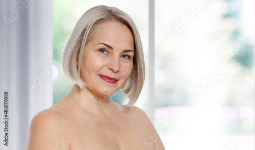Beautiful middle-aged blonde woman sitting relaxed near the window. Selective focus on face. Realistic images with their own imperfections. © missty
