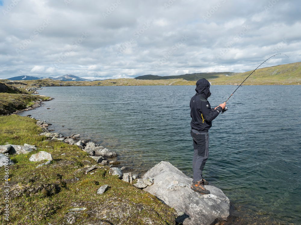 Fisherman, angler figure at northern landscape, tundra in Swedish Lapland with blue artic lake, green hills and mountains. Fishing at Padjelantaleden hiking trail. Summer day, blue sky, white clouds Fisherman, angler figure at northern landscape, tundra in Swedish Lapland with blue artic lake, green hills and mountains. Fishing at Padjelantaleden hiking trail. Summer day, blue sky, white clouds