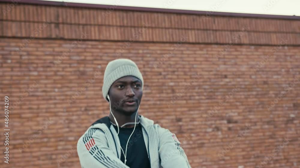 Athletic black man is lifting weight outdoor on a sunny day. He is wearing unbranded sports clothes and headphones. Brick wall on the background. 4k slow motion video. Athletic black man is lifting weight outdoor on a sunny day. He is wearing unbranded sports clothes and headphones. Brick wall on the background. 4k slow motion video.