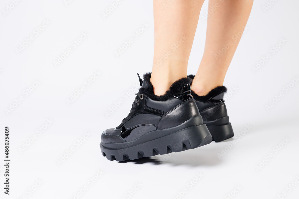 Fashionable black sneakers on the legs of a woman in the studio on a white background. Legs of a young girl with beautiful trendy shoes Fashionable black sneakers on the legs of a woman in the studio on a white background. Legs of a young girl with beautiful trendy shoes