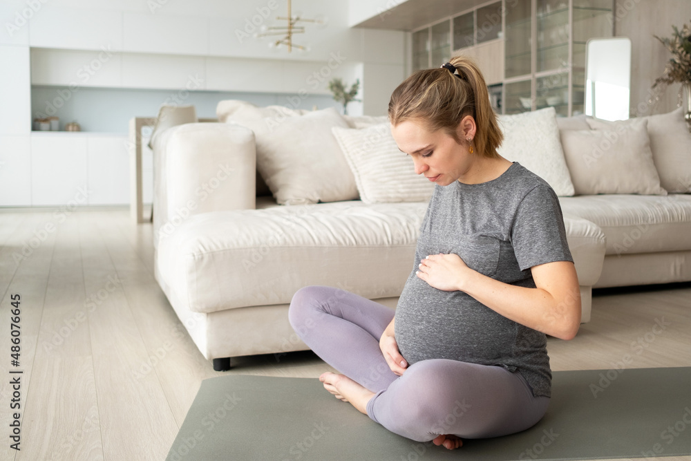 A pregnant woman in the living room of the house does gymnastics for pregnant women. Fitness during pregnancy. A pregnant woman in the living room of the house does gymnastics for pregnant women. Fitness during pregnancy.