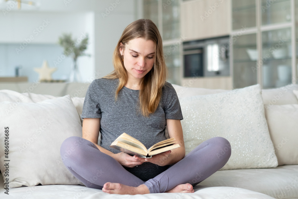 Pregnant woman sitting on the sofa in her living room reading a book. Pregnant woman sitting on the sofa in her living room reading a book.