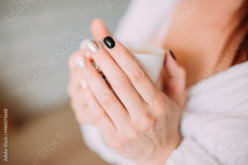 a girl with a black and white manicure holds a cup of milk in her hands