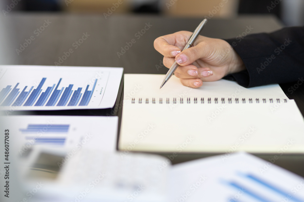 Fototapeta premium Businesswoman working on her desk holding a pen and writing a note on a notepad.