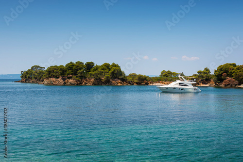 Panoramic photo of the turquoise sea with a white yacht docked in the bay on a summer day in Greece