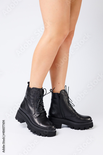 Woman in trendy black shoes on a white background, close-up. Woman's legs in stylish leather shoes