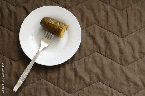 Pickled cucumber on a fork on a white saucer on a brown background.