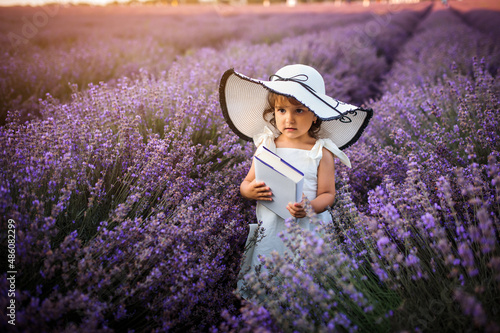 Girl child in white dress and white big hat is smiling in the lavender field.