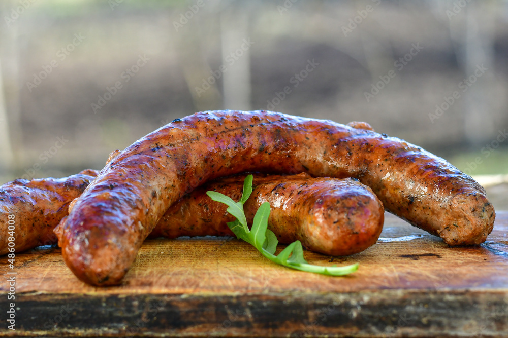 Fototapeta premium Grilled pork juicy sausages on wooden board outdoors. Grilling food, bbq, barbecue, picnic
