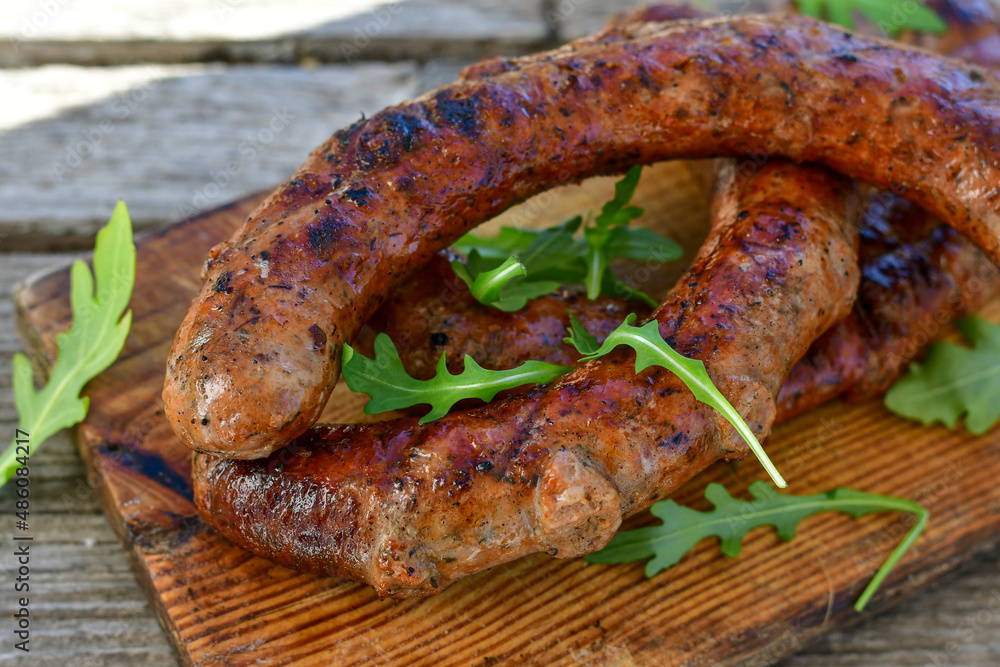Grilled pork juicy sausages on wooden board outdoors. Grilling food, bbq, barbecue, picnic Grilled pork juicy sausages on wooden board outdoors. Grilling food, bbq, barbecue, picnic
