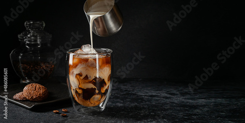Iced coffee with pouring cream on dark stone background. Copy space