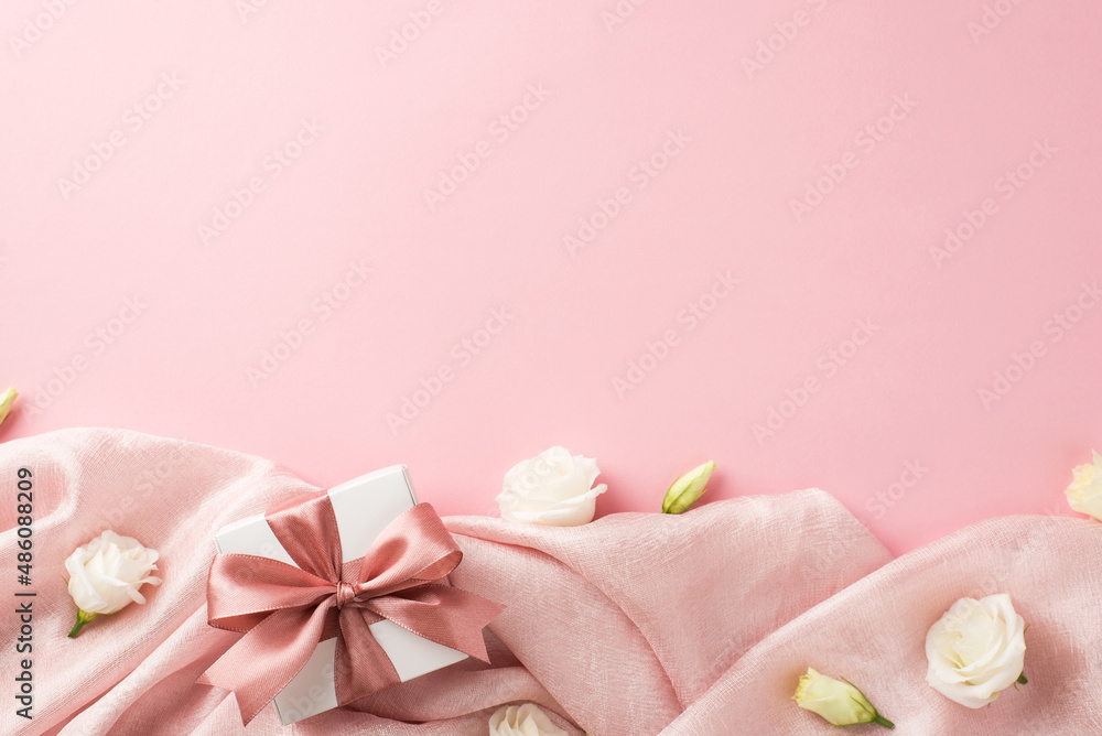 Top view photo of woman's day composition white giftbox with pink satin ribbon bow and white prairie gentian flower buds on soft pink textile on isolated pastel pink background with empty space