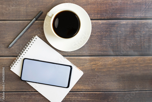 Smartphone with a notepad and a cup of strong coffee on a wooden background. Place for text