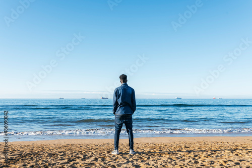 african man on the beach looking at the ocean from behind nostalgic. immigrant