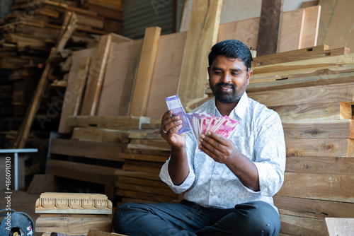 Foucs on face, Happy young indian woodworker or carpenter counting money at workplace or shop - concept of carpentry service, earning, professional occupation, financial and banking. photo