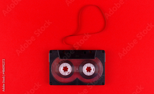 Black audio cassette with pulled out audiotape on red background