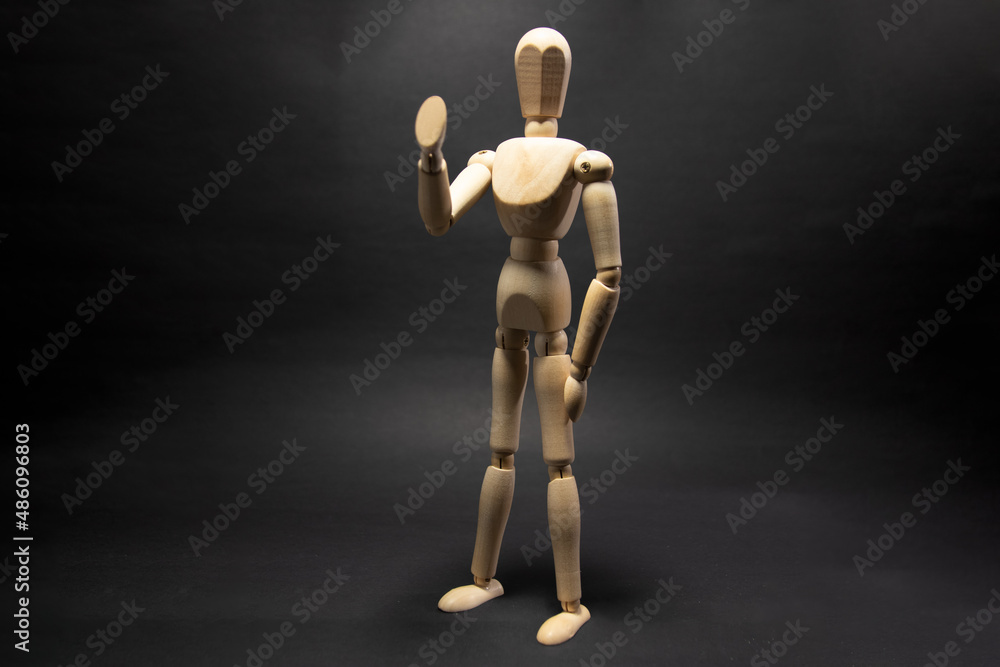 The wooden mannequin raising arm and greets. on a black background The wooden mannequin raising arm and greets. on a black background
